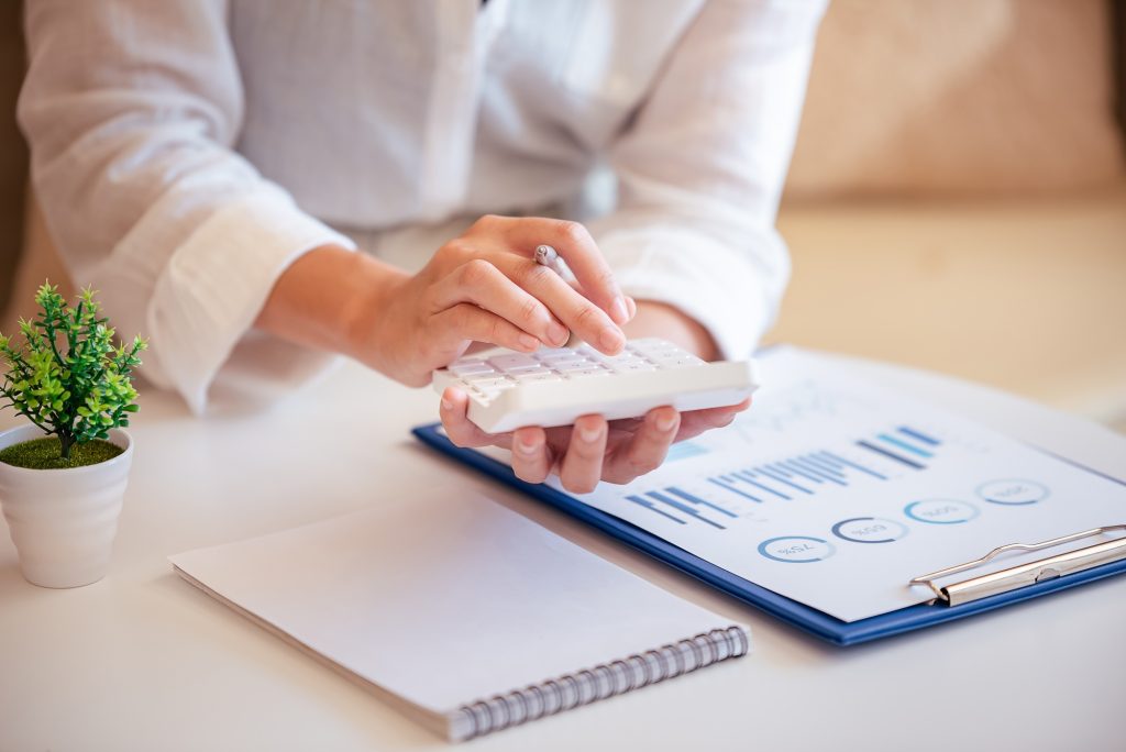 A young woman's hand presses a calculator to determine and summarize the cost of mortgage home loans