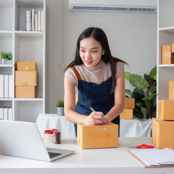 Female Entrepreneur Managing Online Selling Business from Home Office with Shipping Boxes and Laptop